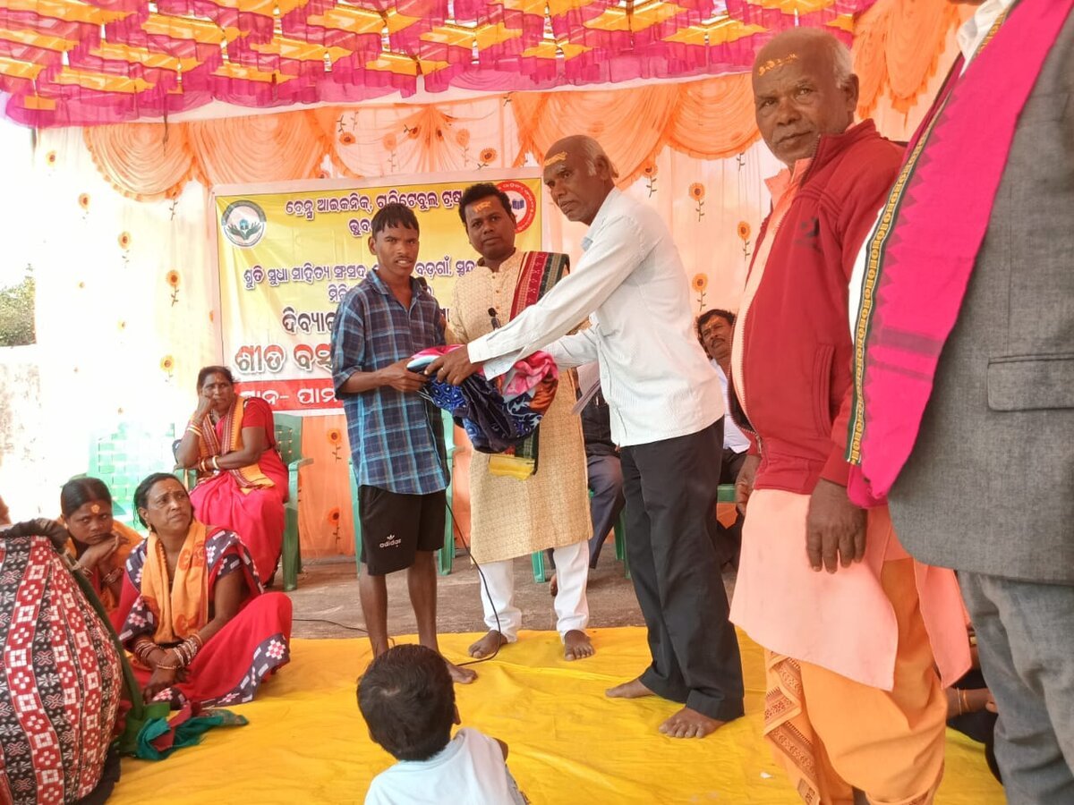 A Brains Iconic Charitable Trust volunteer hands winter clothing to a child during a distribution ceremony.
